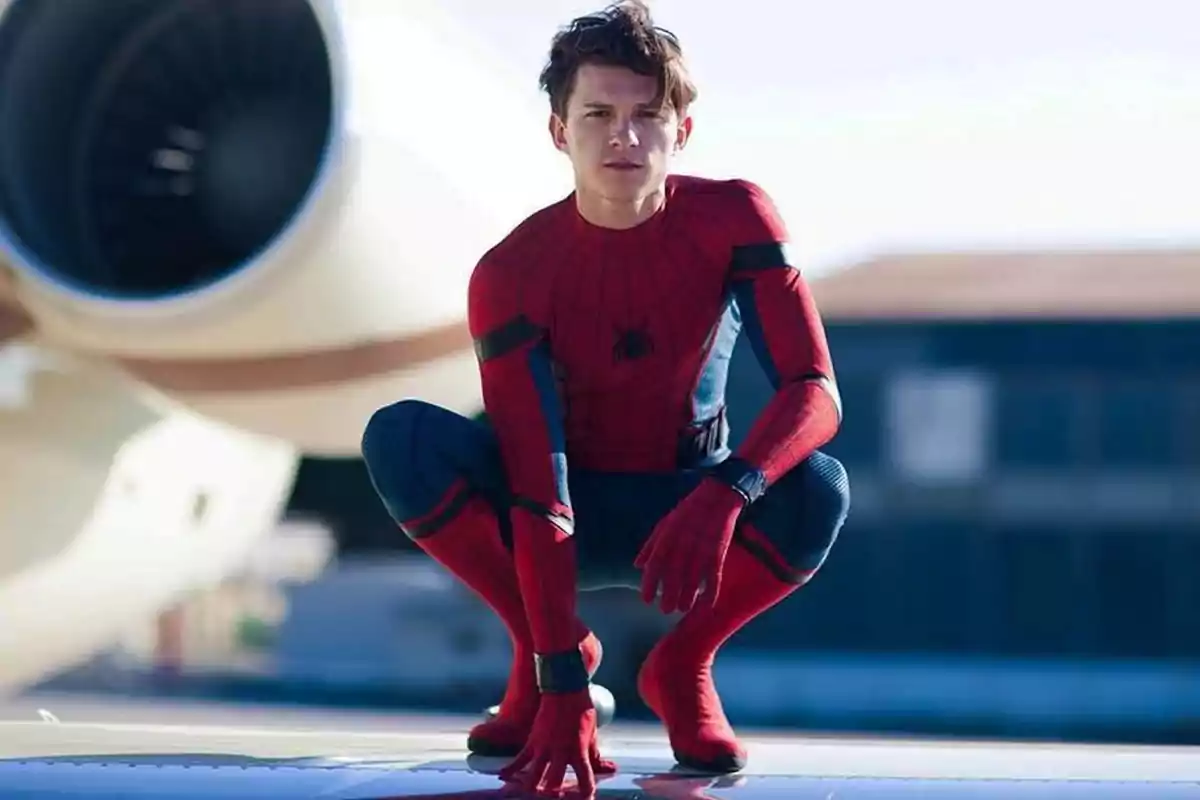 Un joven vestido con el traje de Spider-Man está agachado sobre una superficie metálica con un avión de fondo. Un joven vestido con el traje de Spider-Man está agachado sobre una superficie metálica con un avión de fondo.