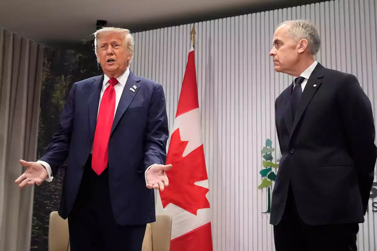 Two men in suits are talking in front of a Canadian flag in a formal setting.