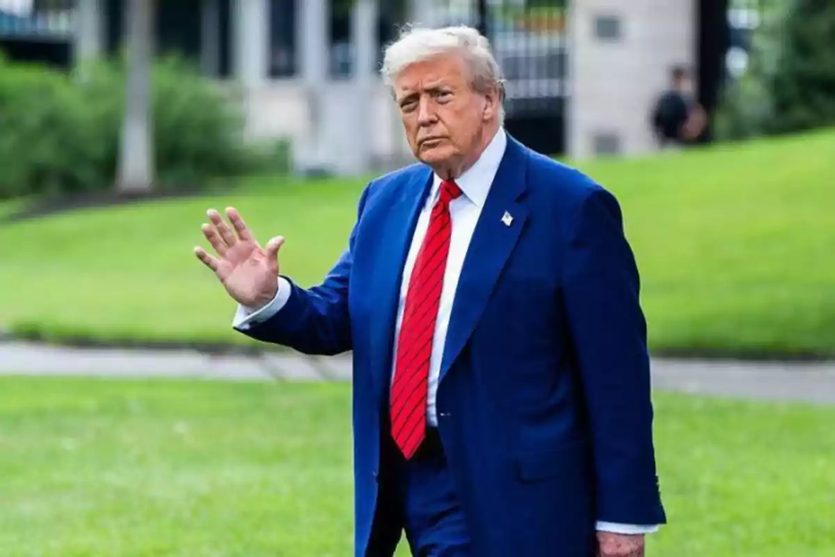 Hombre de cabello canoso con traje azul y corbata roja caminando sobre césped y saludando con la mano derecha. Hombre de cabello canoso con traje azul y corbata roja caminando sobre césped y saludando con la mano derecha.
