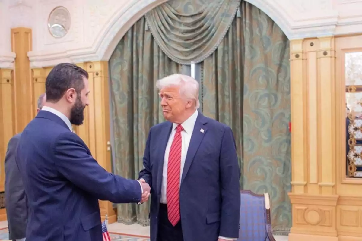 Two men in suits shake hands in an elegant room with green curtains and gold details. Two men in suits shake hands in an elegant room with green curtains and gold details.