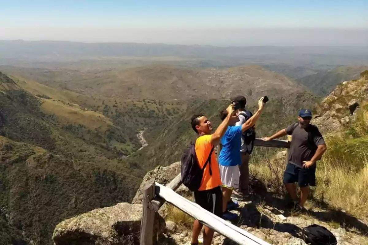 Group of people taking photos and enjoying a panoramic view at the top of a mountain surrounded by vegetation and hills Group of people taking photos and enjoying a panoramic view at the top of a mountain surrounded by vegetation and hills