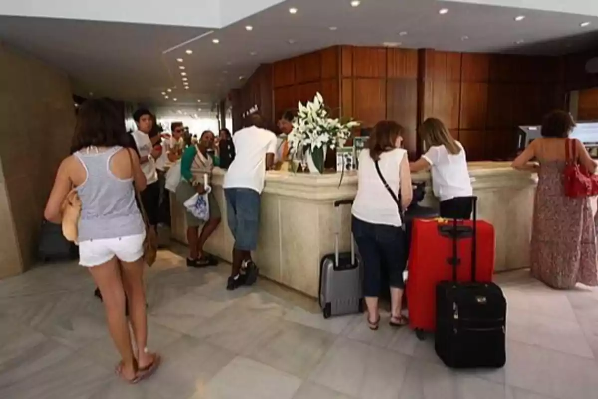 People standing in line at a hotel reception with suitcases and white flowers on the counter