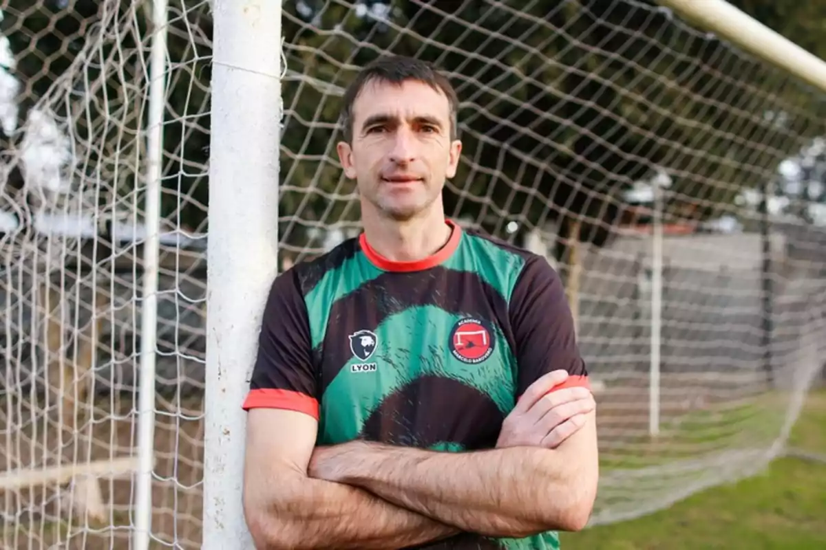 Hombre con camiseta deportiva de fútbol apoyado en un poste de la portería en una cancha al aire libre Hombre con camiseta deportiva de fútbol apoyado en un poste de la portería en una cancha al aire libre
