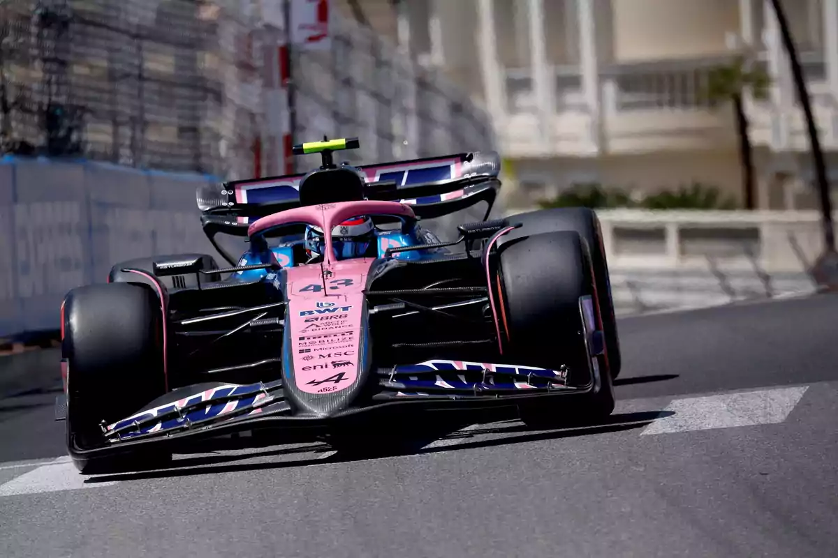A pink and blue Formula 1 car drives on a city track during a race. A pink and blue Formula 1 car drives on a city track during a race.