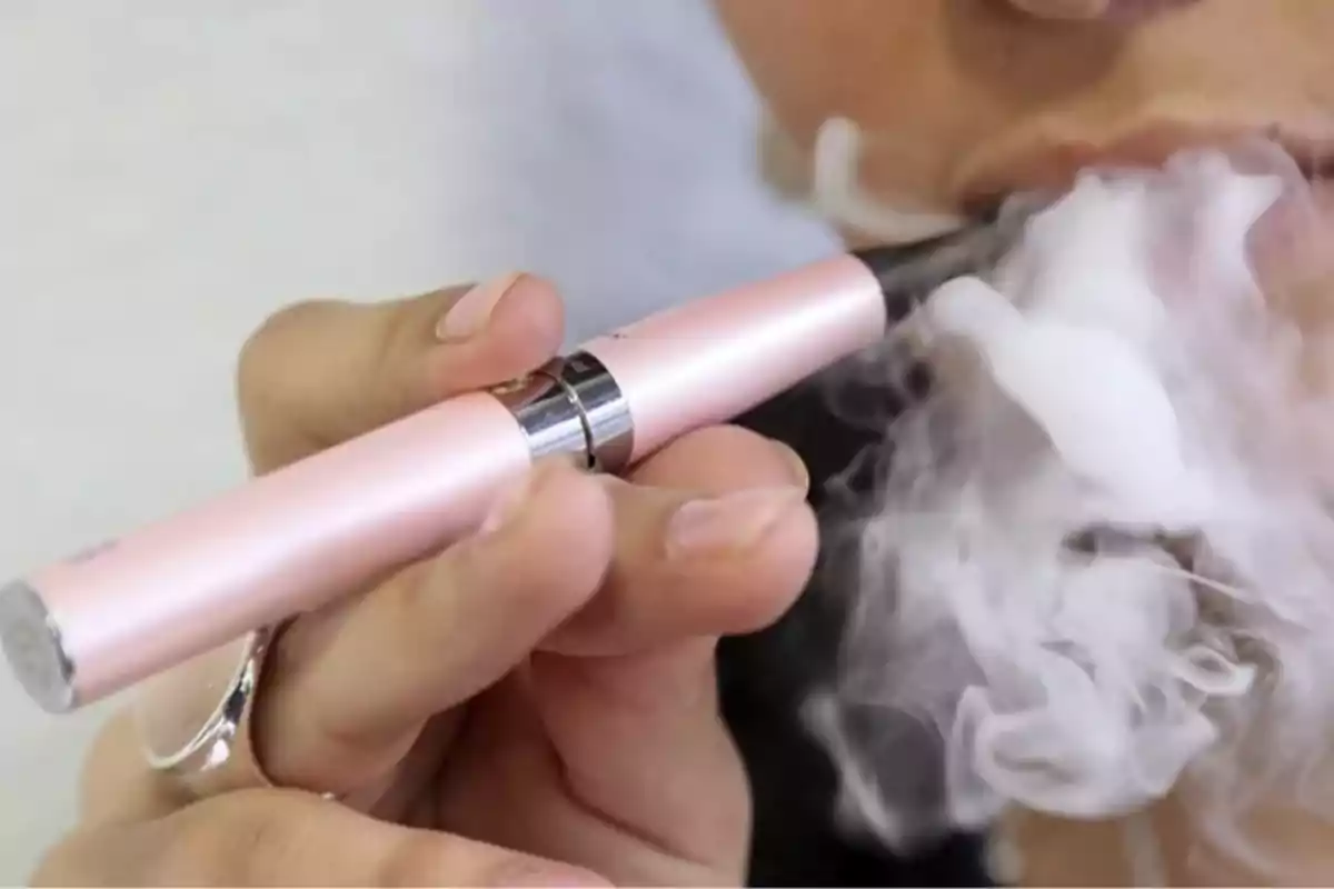 Persona usando un cigarro electrónico color rosa mientras exhala vapor Persona usando un cigarro electrónico color rosa mientras exhala vapor