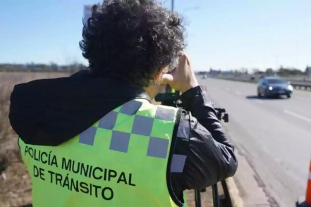 Agente de tránsito con chaleco amarillo observando una carretera mientras mide la velocidad de los autos que circulan