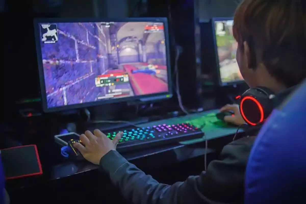 Person playing video games on a computer with a backlit keyboard and headphones with red lights Person playing video games on a computer with a backlit keyboard and headphones with red lights