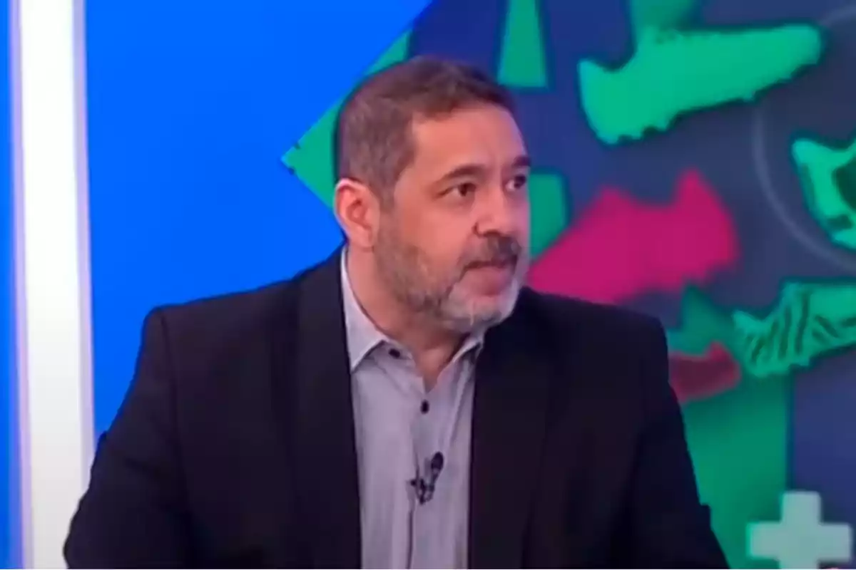 Hombre de cabello corto y barba con saco oscuro y camisa clara participando en un programa de televisión con fondo colorido. Hombre de cabello corto y barba con saco oscuro y camisa clara participando en un programa de televisión con fondo colorido.