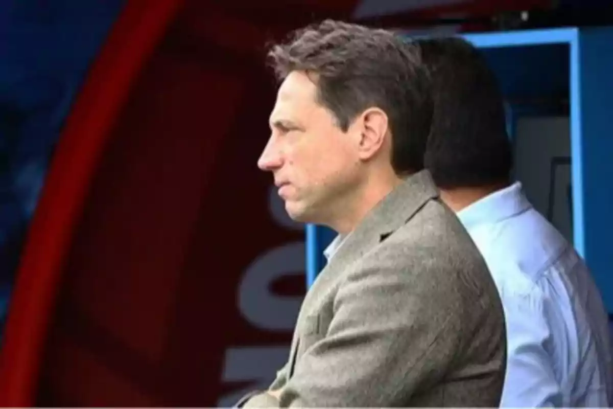 Man in profile wearing a gray jacket, watching alertly in a sports setting