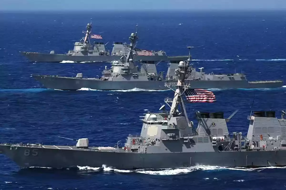 Three warships sailing in formation on the sea with United States flags waving