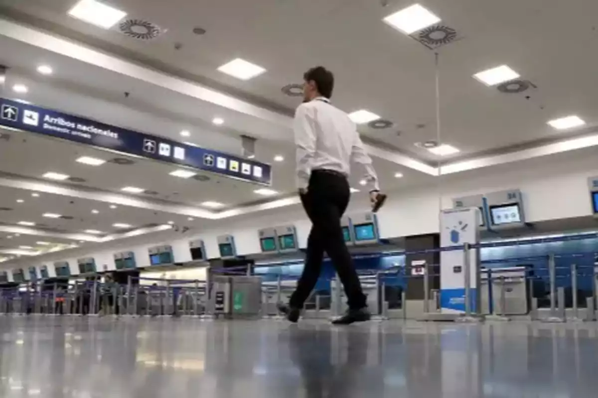 Hombre caminando en el área de mostradores de un aeropuerto moderno y vacío Hombre caminando en el área de mostradores de un aeropuerto moderno y vacío