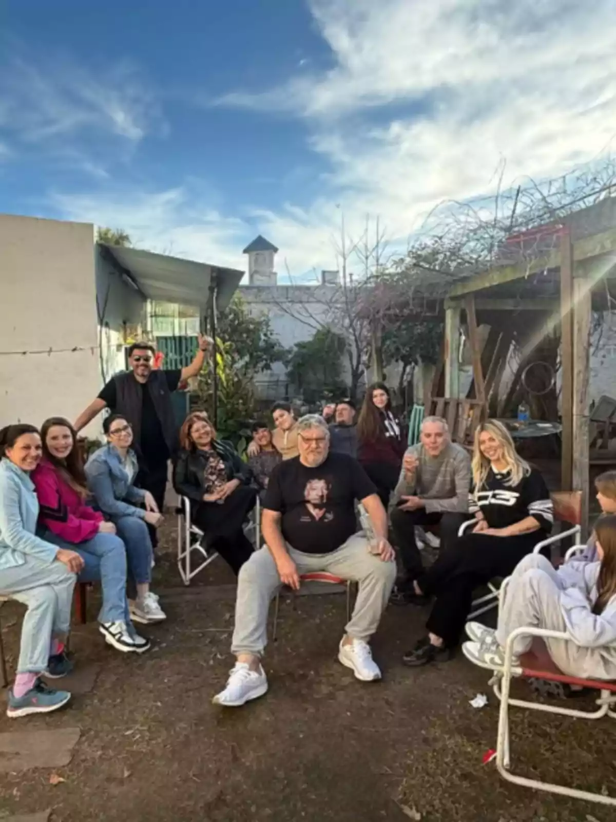 Un grupo de personas sonríe y conversa sentados en un patio al aire libre en un día soleado Un grupo de personas sonríe y conversa sentados en un patio al aire libre en un día soleado