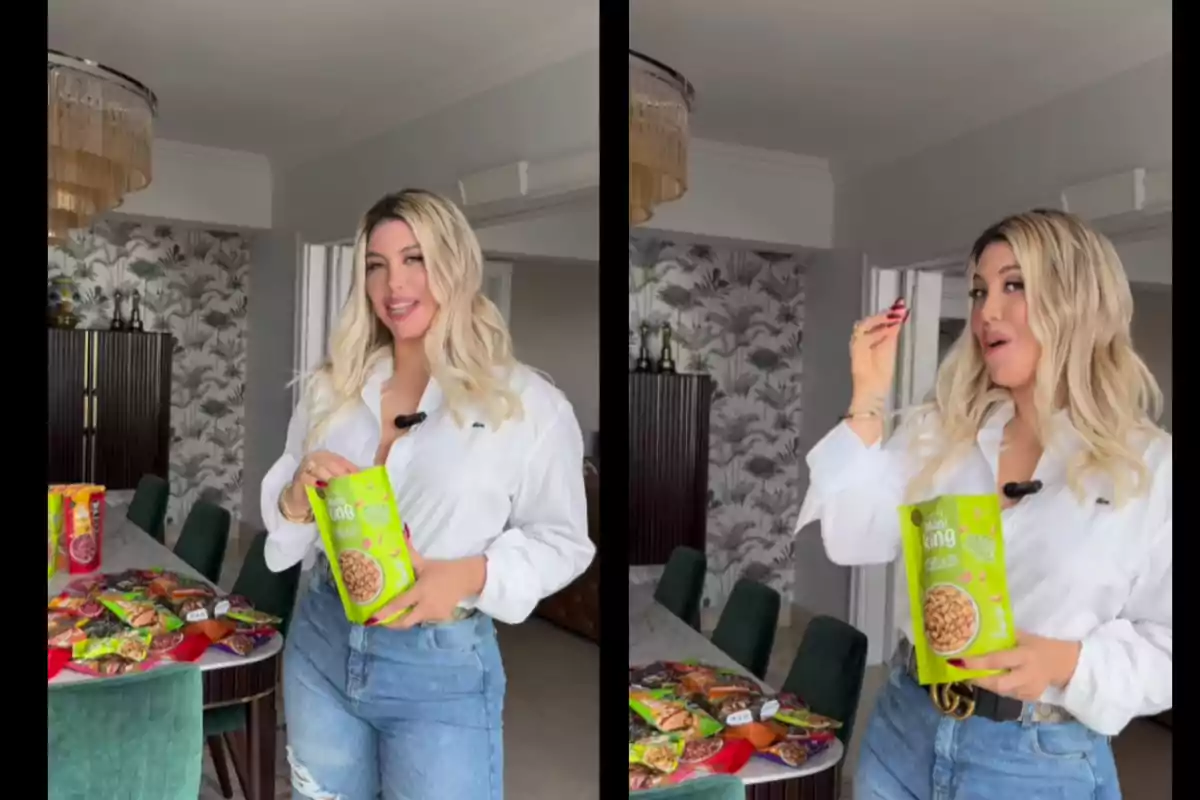 Blonde woman in a white jersey and jeans holds a green snack bag while smiling and tasting the product in a modern kitchen with a table full of assorted snacks. Blonde woman in a white jersey and jeans holds a green snack bag while smiling and tasting the product in a modern kitchen with a table full of assorted snacks.
