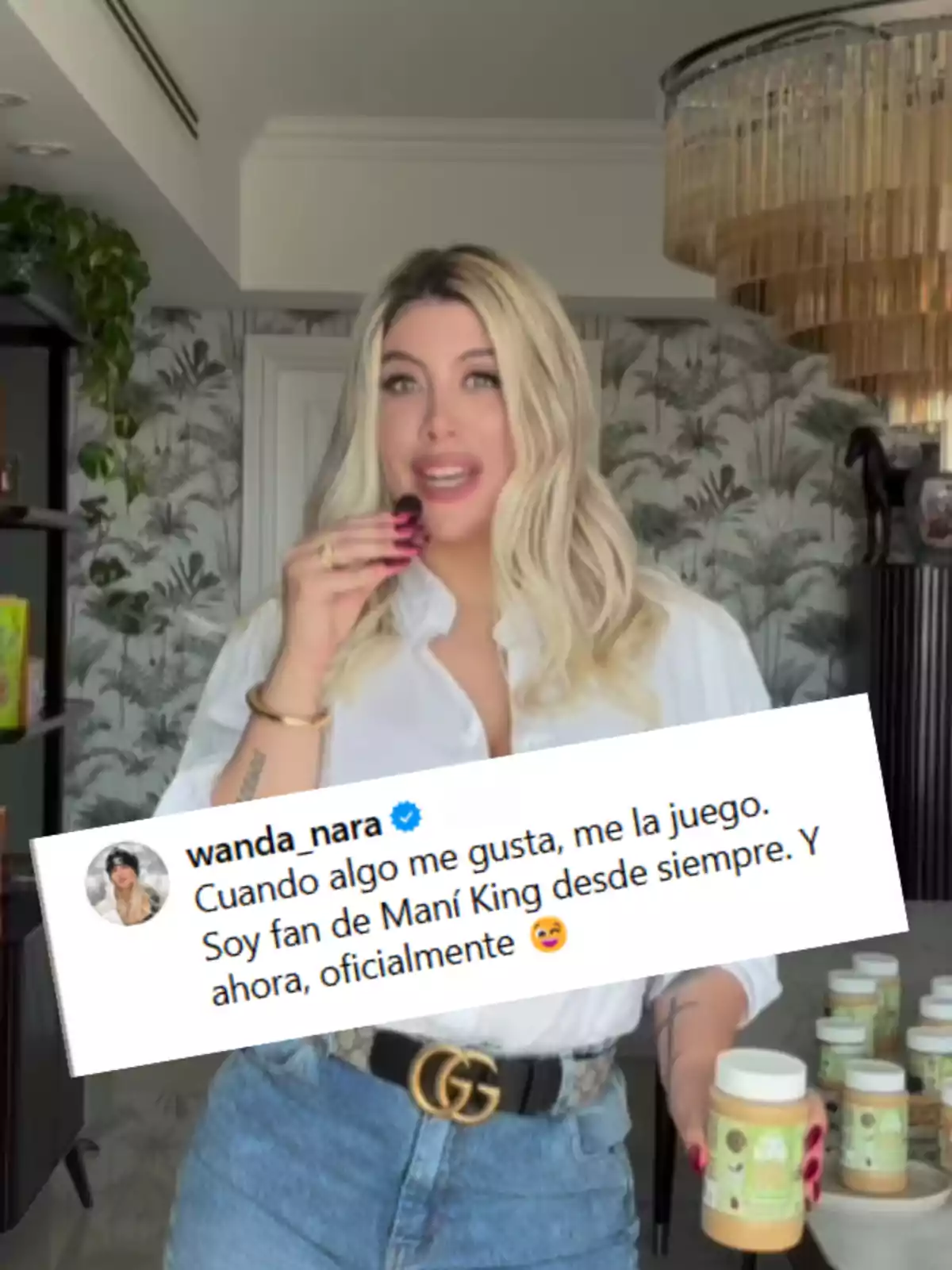 Mujer rubia con camisa blanca y jeans sostiene un frasco de crema de maní en una cocina moderna mientras muestra un mensaje promocional sobre su fanatismo por la marca Mani King Mujer rubia con camisa blanca y jeans sostiene un frasco de crema de maní en una cocina moderna mientras muestra un mensaje promocional sobre su fanatismo por la marca Mani King