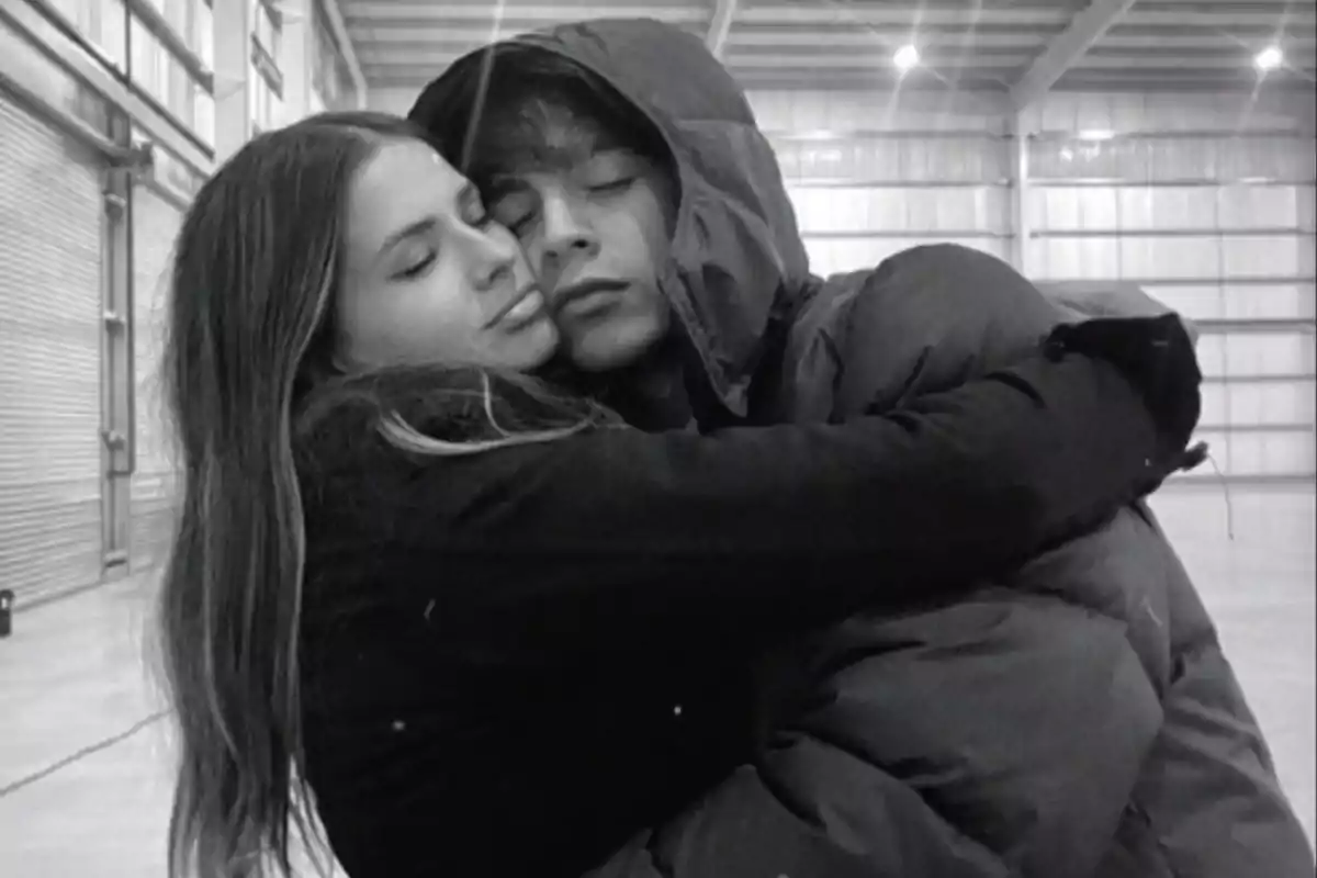 Two young people embrace with their eyes closed in what appears to be a warehouse or hangar, conveying a sense of affection and tranquility. Two young people embrace with their eyes closed in what appears to be a warehouse or hangar, conveying a sense of affection and tranquility.