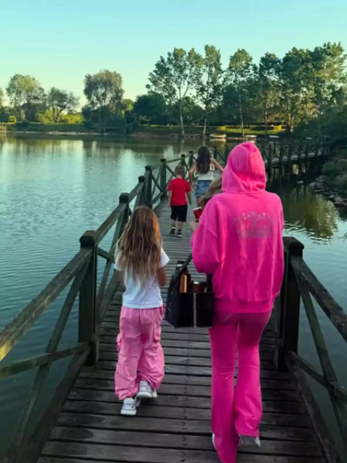 Several people are walking on a wooden bridge that crosses a lake surrounded by trees on a sunny day. Several people are walking on a wooden bridge that crosses a lake surrounded by trees on a sunny day.