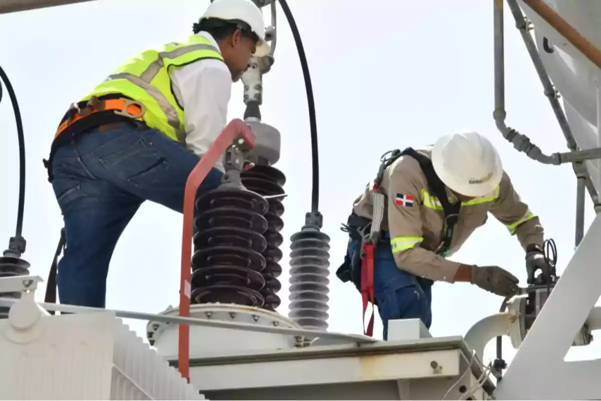 Dos trabajadores con casco y chaleco de seguridad realizan labores de mantenimiento en una estructura eléctrica Dos trabajadores con casco y chaleco de seguridad realizan labores de mantenimiento en una estructura eléctrica