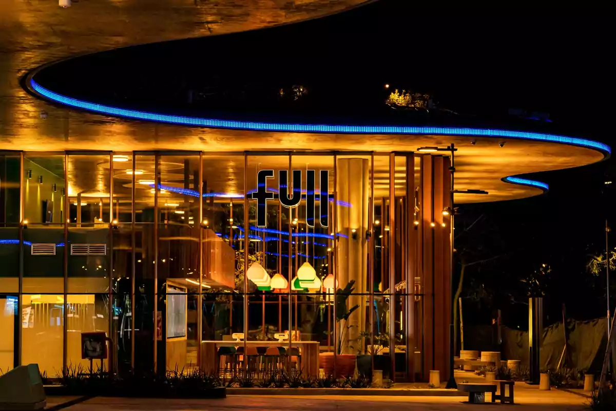 Facade of a modern restaurant with a curved illuminated roof and large glass windows at night