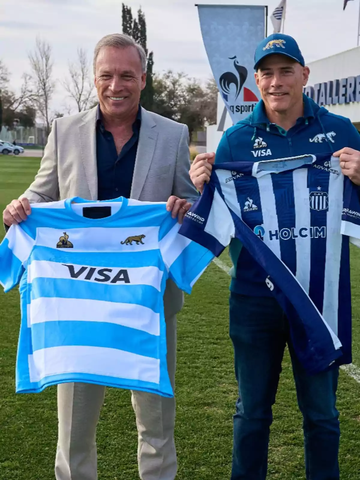 Two smiling men pose on a grass field holding sports jerseys from different teams. Two smiling men pose on a grass field holding sports jerseys from different teams.