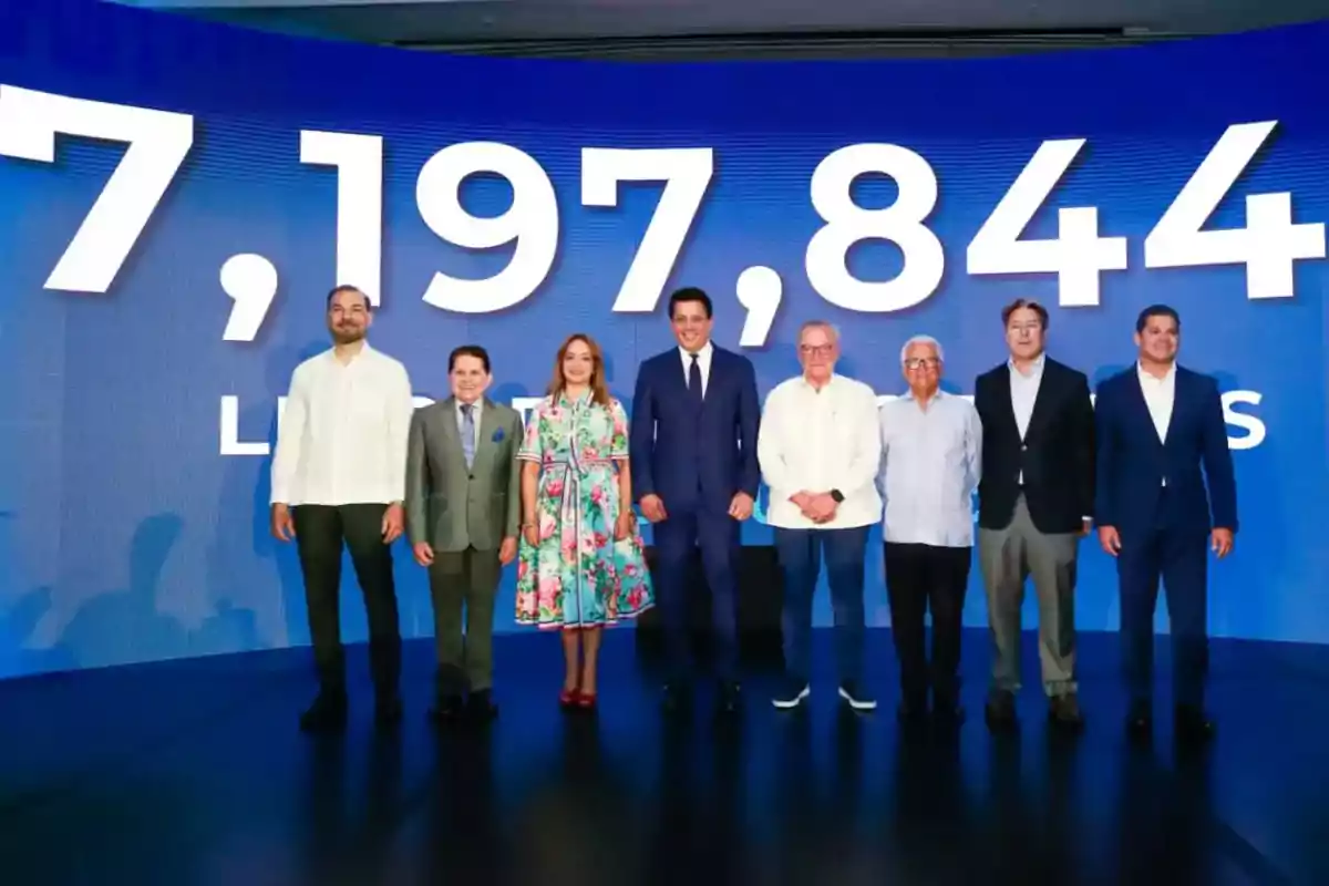 Ocho personas posan de pie frente a una pantalla azul con números grandes en color blanco