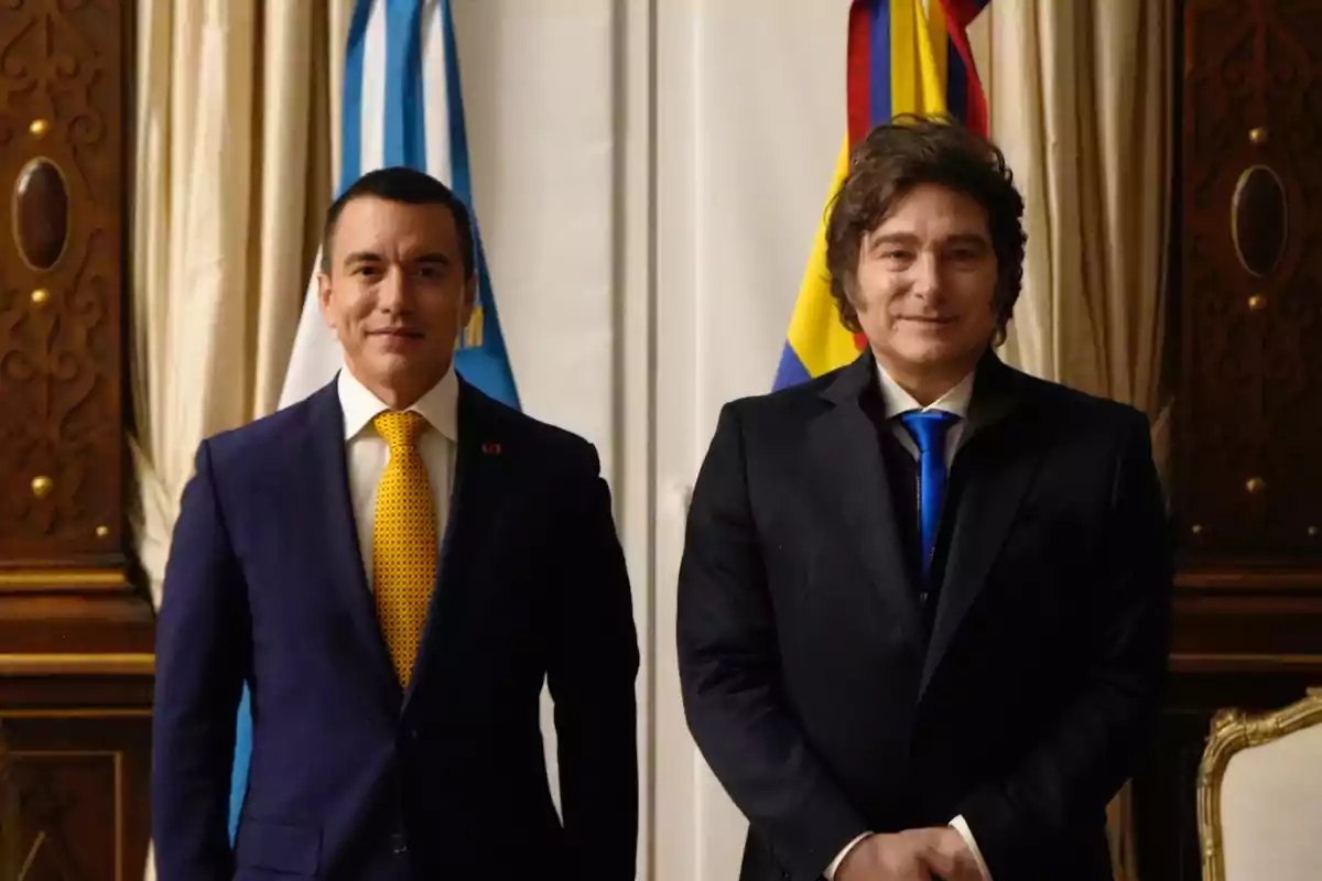 Dos hombres con traje posan juntos en un salón elegante con banderas de Argentina y Colombia al fondo Dos hombres con traje posan juntos en un salón elegante con banderas de Argentina y Colombia al fondo