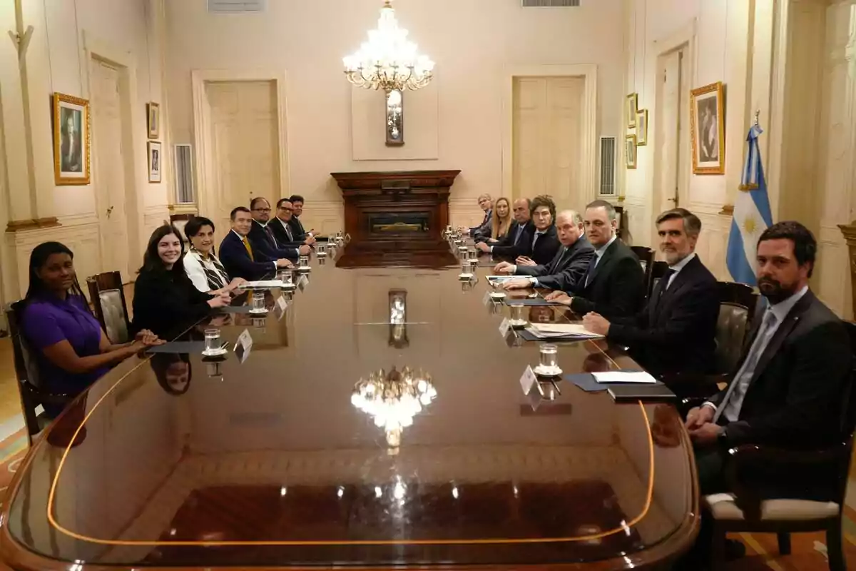 Personas sentadas alrededor de una mesa larga en una sala elegante con una bandera de Argentina al fondo Personas sentadas alrededor de una mesa larga en una sala elegante con una bandera de Argentina al fondo
