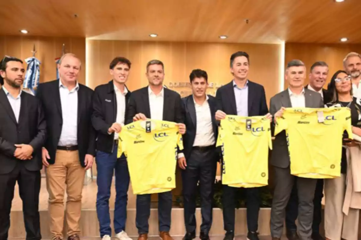 Group of people posing at a formal event while some hold yellow t-jerseys Group of people posing at a formal event while some hold yellow t-jerseys