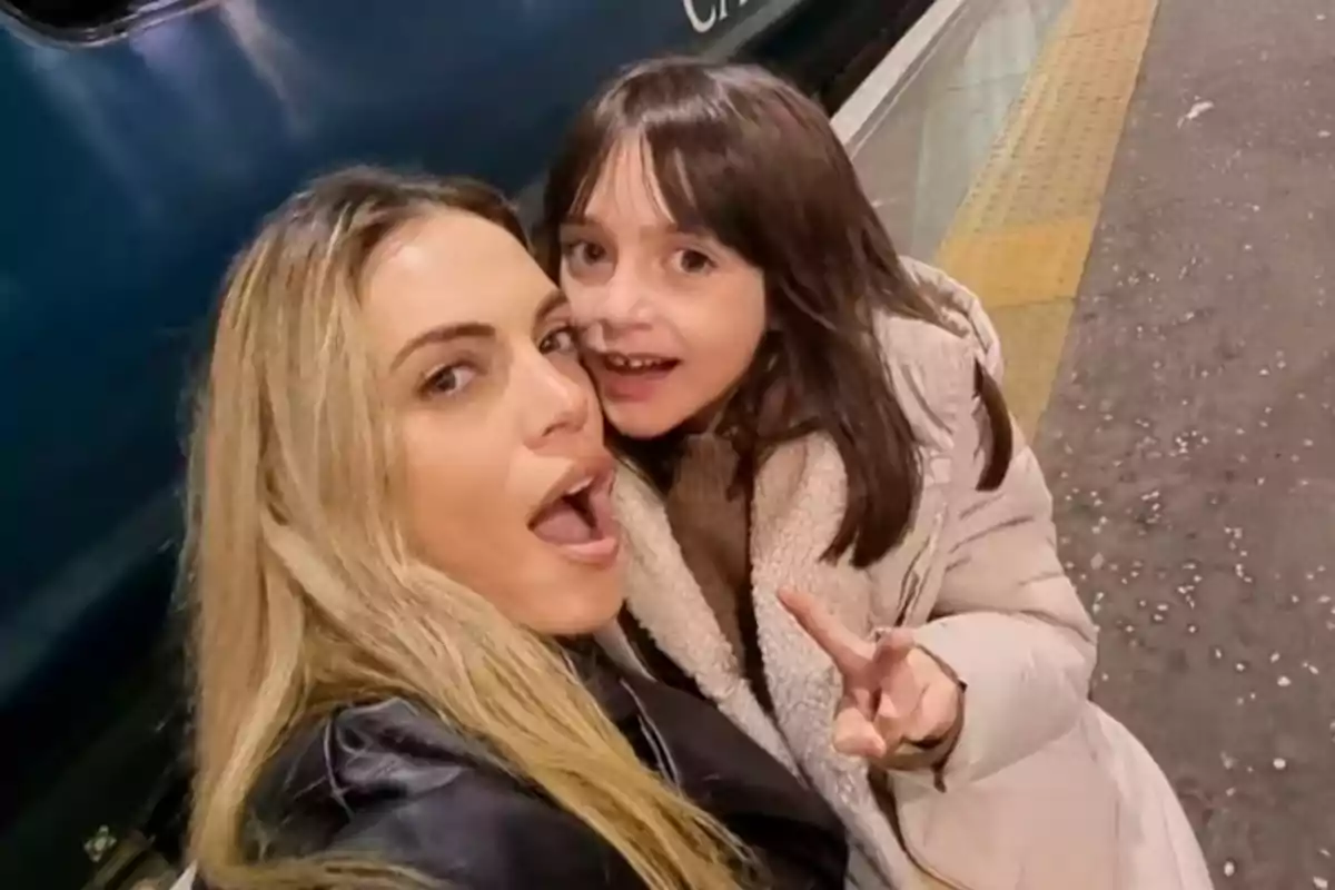 Woman and girl smile and pose for a selfie on a platform next to a train, the girl making a peace sign with her fingers. Woman and girl smile and pose for a selfie on a platform next to a train, the girl making a peace sign with her fingers.