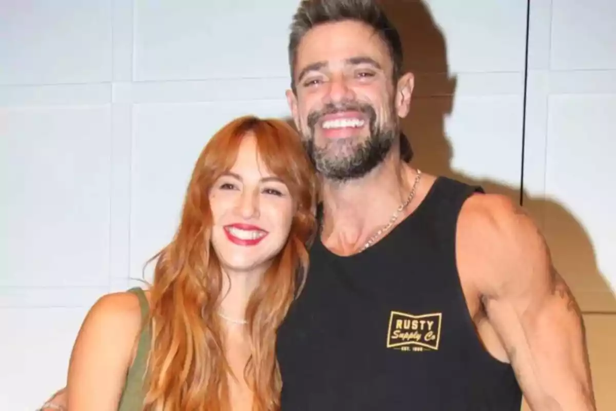 Una pareja sonriente posa abrazada frente a una pared clara Una pareja sonriente posa abrazada frente a una pared clara