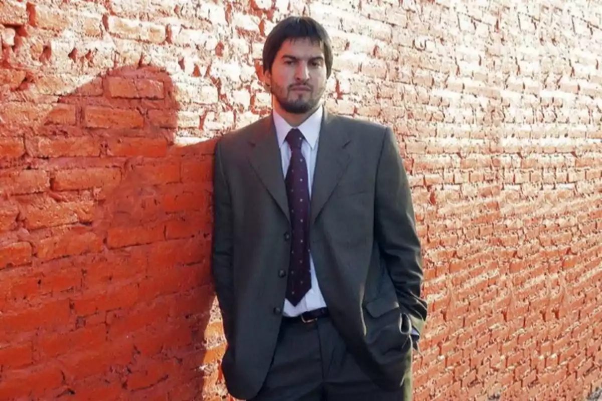 Hombre con traje apoyado en una pared de ladrillos rojos