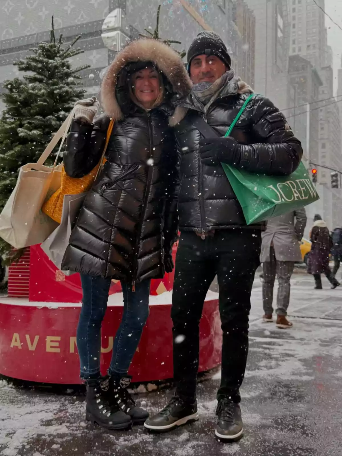 Bundled-up couple smiling while posing on a snowy city street with shopping bags and Christmas trees in the background Bundled-up couple smiling while posing on a snowy city street with shopping bags and Christmas trees in the background