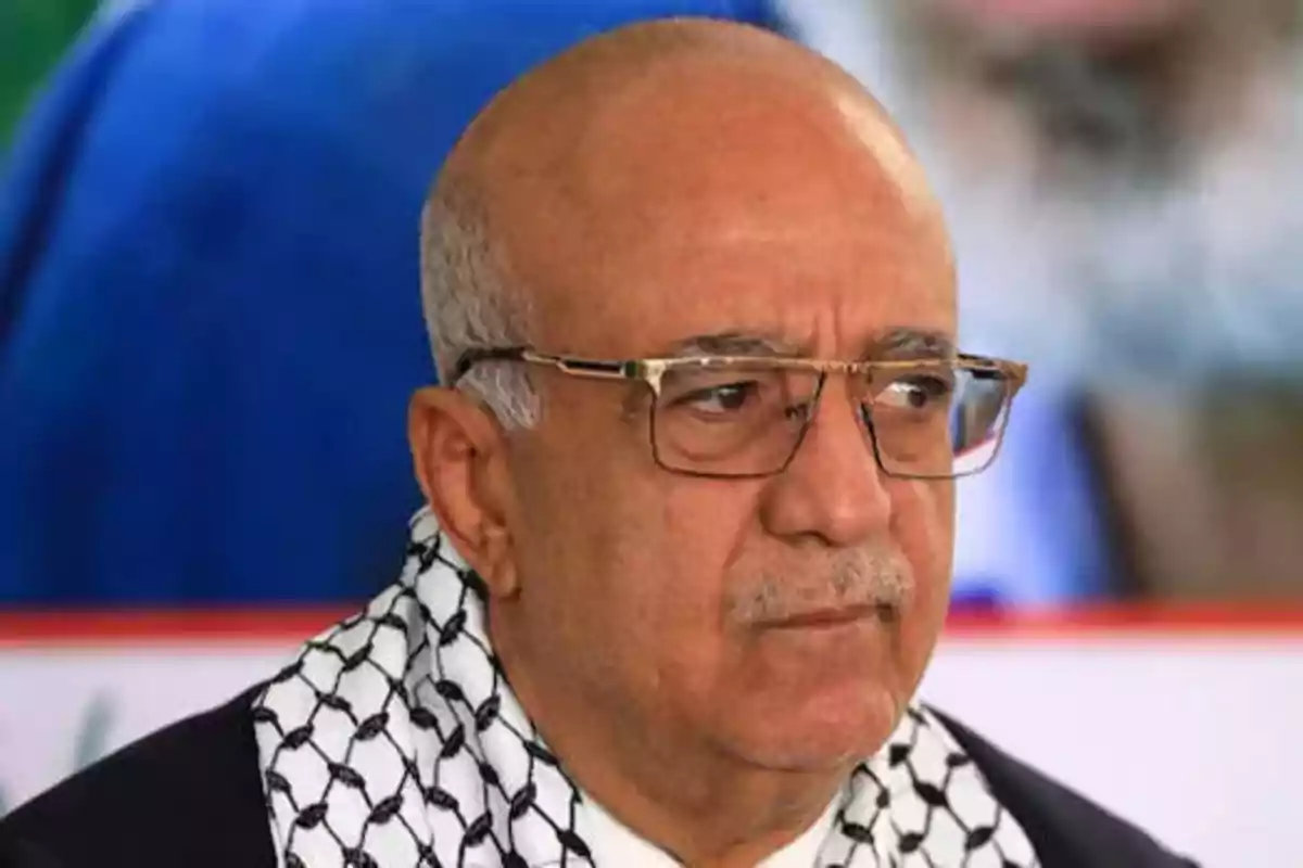 Bald older man with glasses and a black and white patterned scarf looking to the side