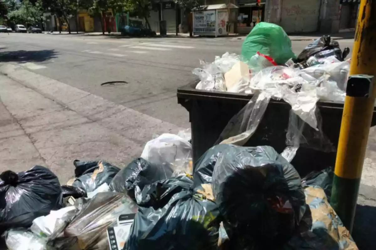Overflowing trash container with bags and waste piled up on an urban street Overflowing trash container with bags and waste piled up on an urban street