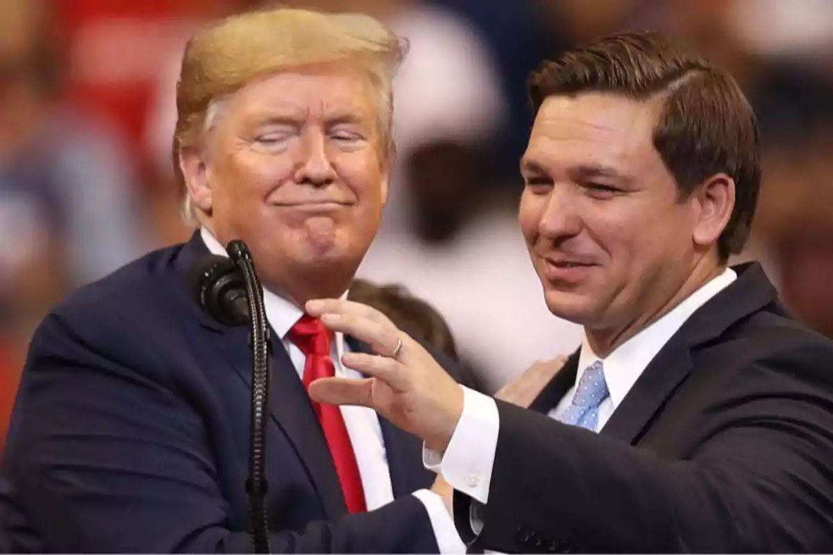 Two men in suits smile and greet each other at a public event in front of a microphone.