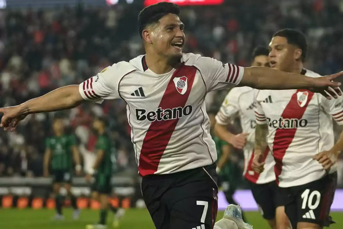 River Plate player celebrating a goal with arms outstretched while his teammates run behind him in the stadium