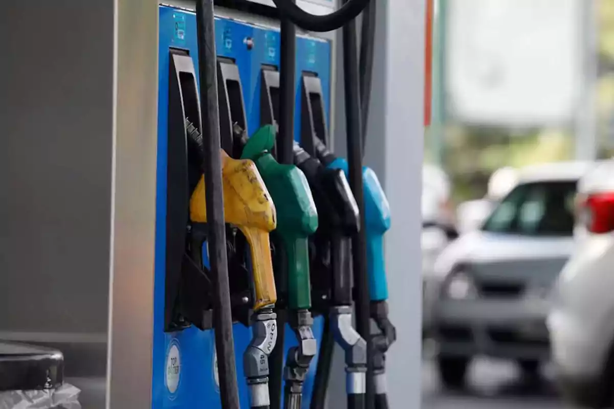 Surtidores de gasolina de diferentes colores en una estación de servicio con autos al fondo Surtidores de gasolina de diferentes colores en una estación de servicio con autos al fondo