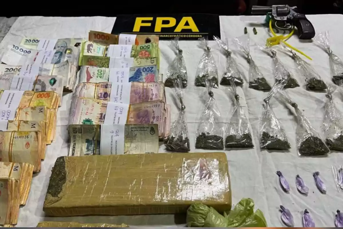 Billetes de diferentes denominaciones, varias bolsas con sustancia vegetal, envoltorios pequeños, un arma de fuego y un cartel de la FPA sobre una mesa blanca Billetes de diferentes denominaciones, varias bolsas con sustancia vegetal, envoltorios pequeños, un arma de fuego y un cartel de la FPA sobre una mesa blanca