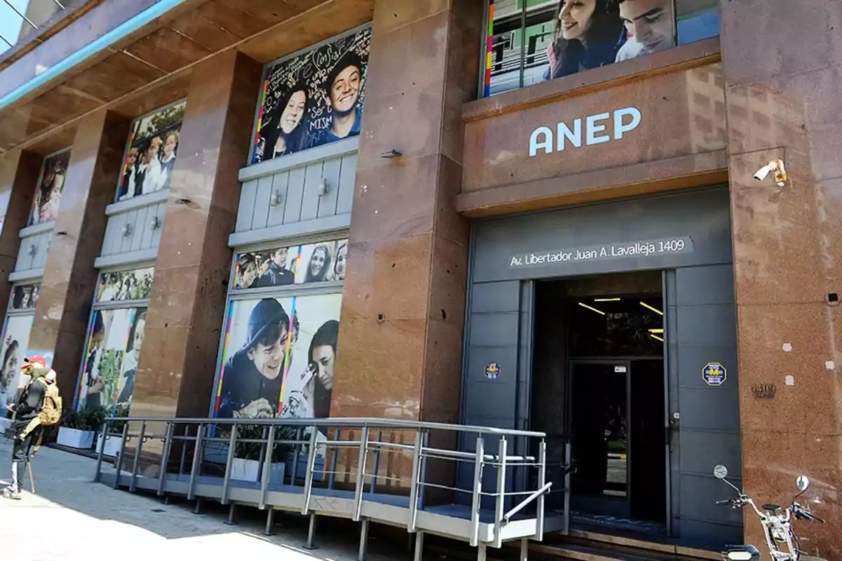 Fachada de un edificio de la ANEP con imágenes de jóvenes en las ventanas y una rampa de acceso en la entrada principal Fachada de un edificio de la ANEP con imágenes de jóvenes en las ventanas y una rampa de acceso en la entrada principal