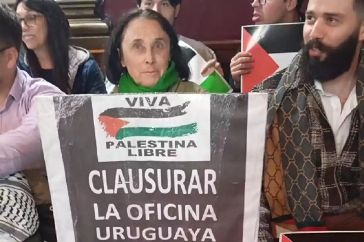 Woman holds a sign calling for the closure of the Uruguayan office and supporting the Free Palestine cause, surrounded by other people at a protest. Woman holds a sign calling for the closure of the Uruguayan office and supporting the Free Palestine cause, surrounded by other people at a protest.