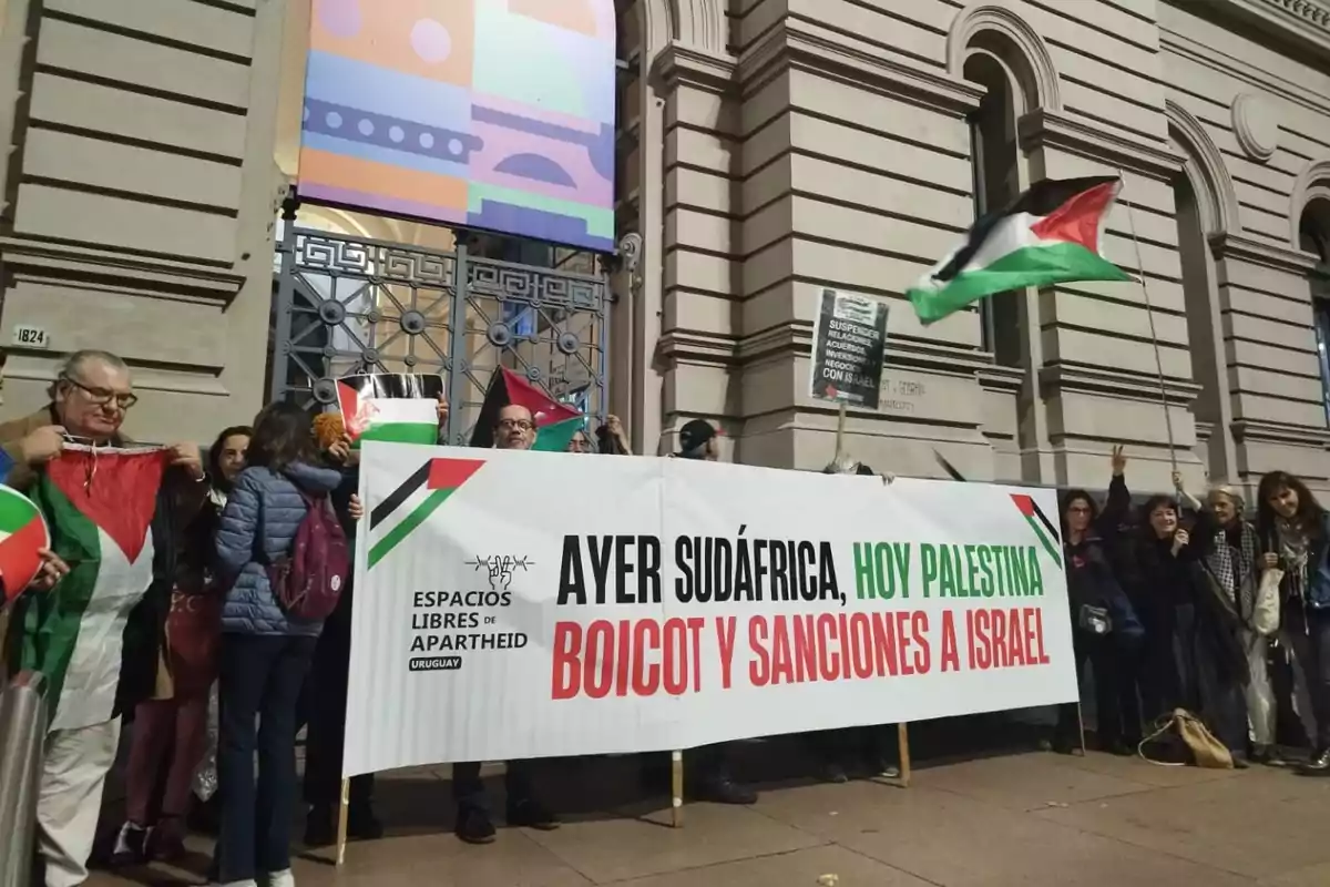 People protesting in front of a building holding Palestinian flags and a banner calling for a boycott and sanctions against Israel in support of Palestine