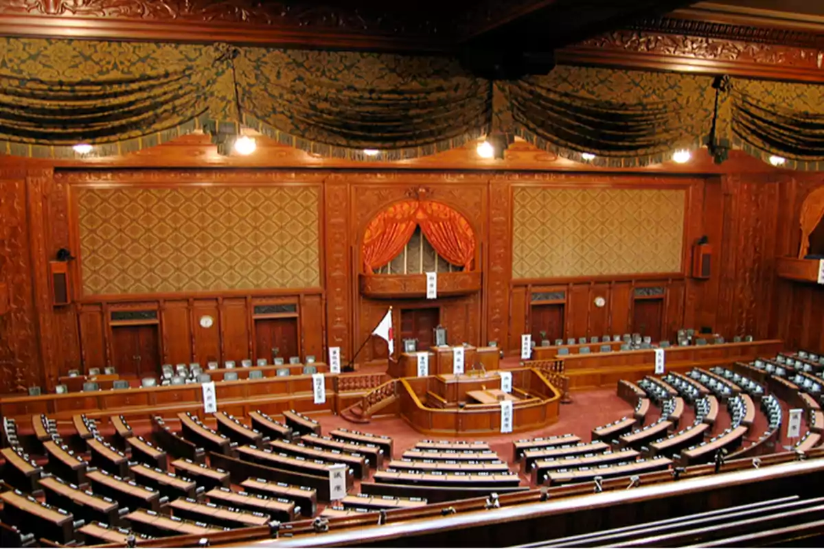 Wood-paneled parliamentary chamber with curved seating and a Japanese flag next to the main podium Wood-paneled parliamentary chamber with curved seating and a Japanese flag next to the main podium