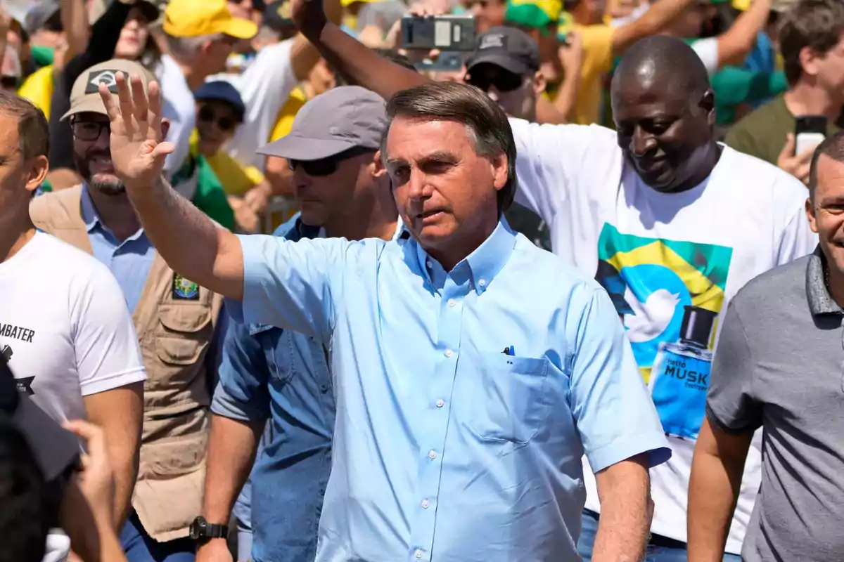 Man in a light blue jersey waves with his hand raised while walking through a crowd of people at an outdoor event Man in a light blue jersey waves with his hand raised while walking through a crowd of people at an outdoor event
