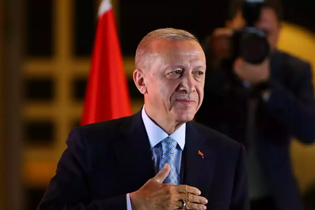 Man in a suit with a blue tie and a red flag in the background while placing his hand on his chest Man in a suit with a blue tie and a red flag in the background while placing his hand on his chest