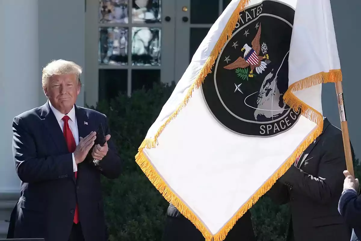 Man in a dark suit applauding next to a white flag with the United States Space Force emblem