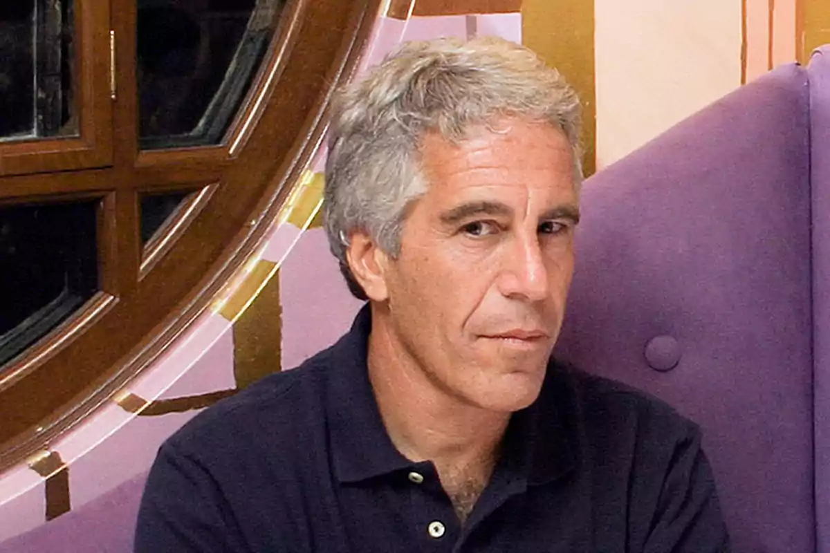 Gray-haired, short-haired man wearing a dark polo jersey sitting in front of a round window and a purple armchair Gray-haired, short-haired man wearing a dark polo jersey sitting in front of a round window and a purple armchair
