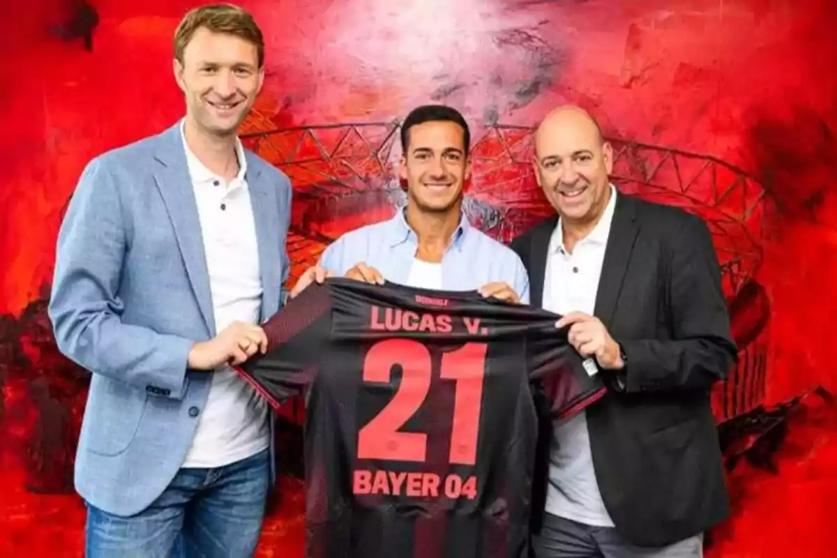 Three men smile while holding a black and red soccer jersey with the name Lucas V and the number 21 in front of a red background. Three men smile while holding a black and red soccer jersey with the name Lucas V and the number 21 in front of a red background.