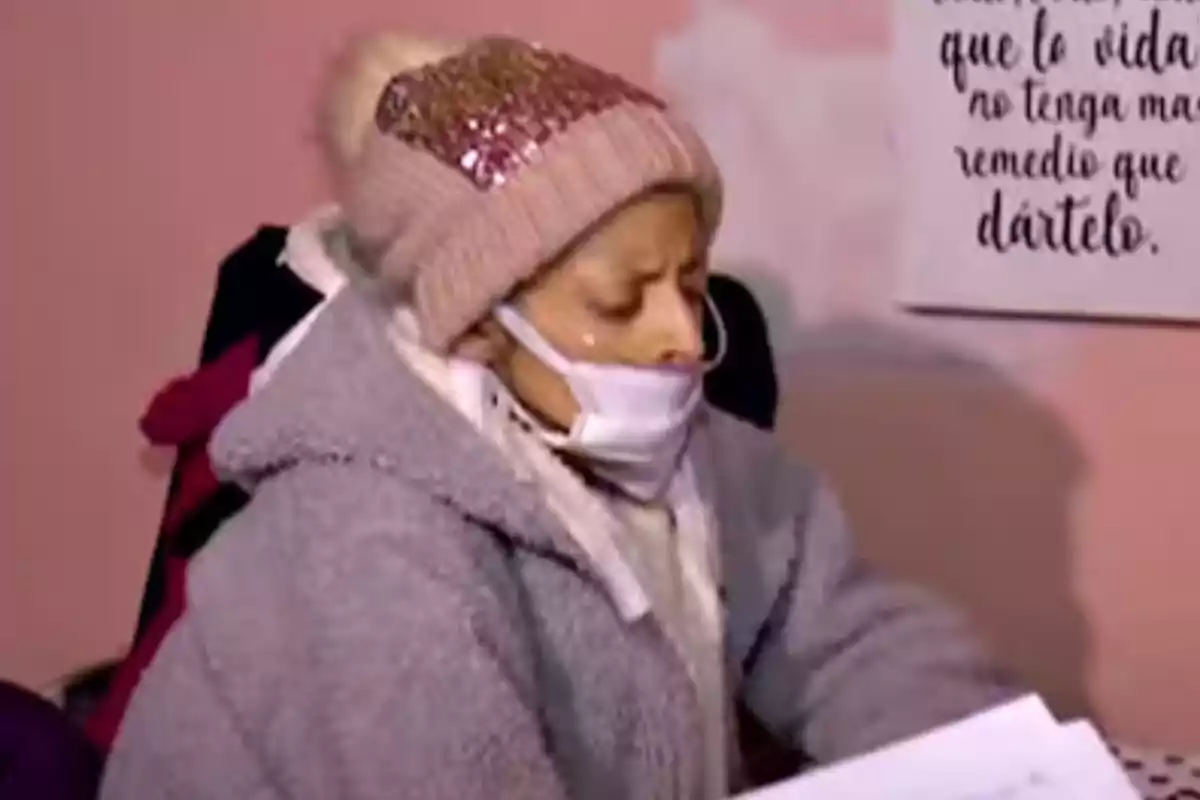 Woman wearing a knit hat and face mask sitting in a pink room going through papers Woman wearing a knit hat and face mask sitting in a pink room going through papers