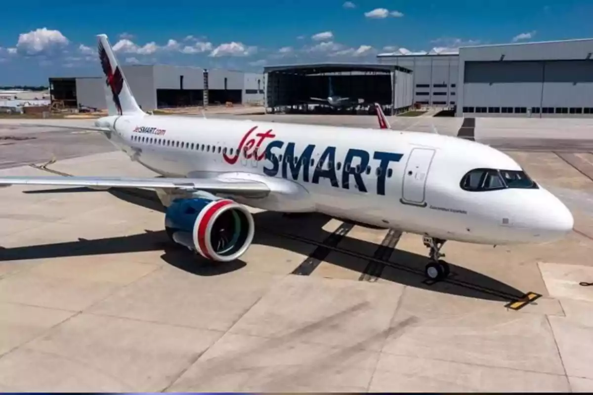 JetSMART airline plane parked on an airport runway with hangars in the background and clear skies. JetSMART airline plane parked on an airport runway with hangars in the background and clear skies.