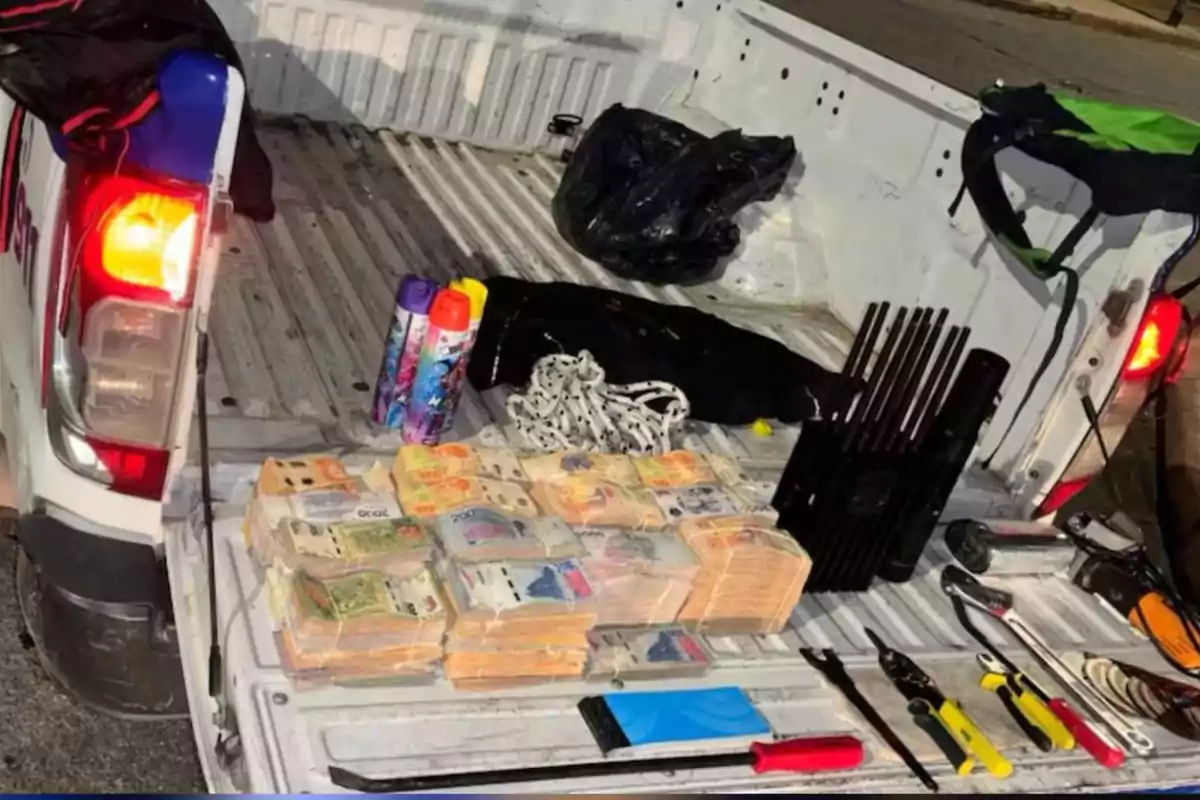 Billetes apilados, herramientas, latas de aerosol y otros objetos sobre la batea de una camioneta blanca Billetes apilados, herramientas, latas de aerosol y otros objetos sobre la batea de una camioneta blanca