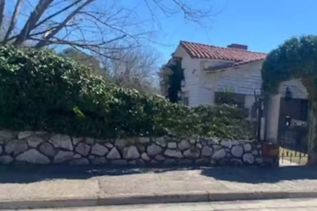 White house with a red tile roof behind a stone wall covered with plants and a leafless tree in the background on a sunny day White house with a red tile roof behind a stone wall covered with plants and a leafless tree in the background on a sunny day